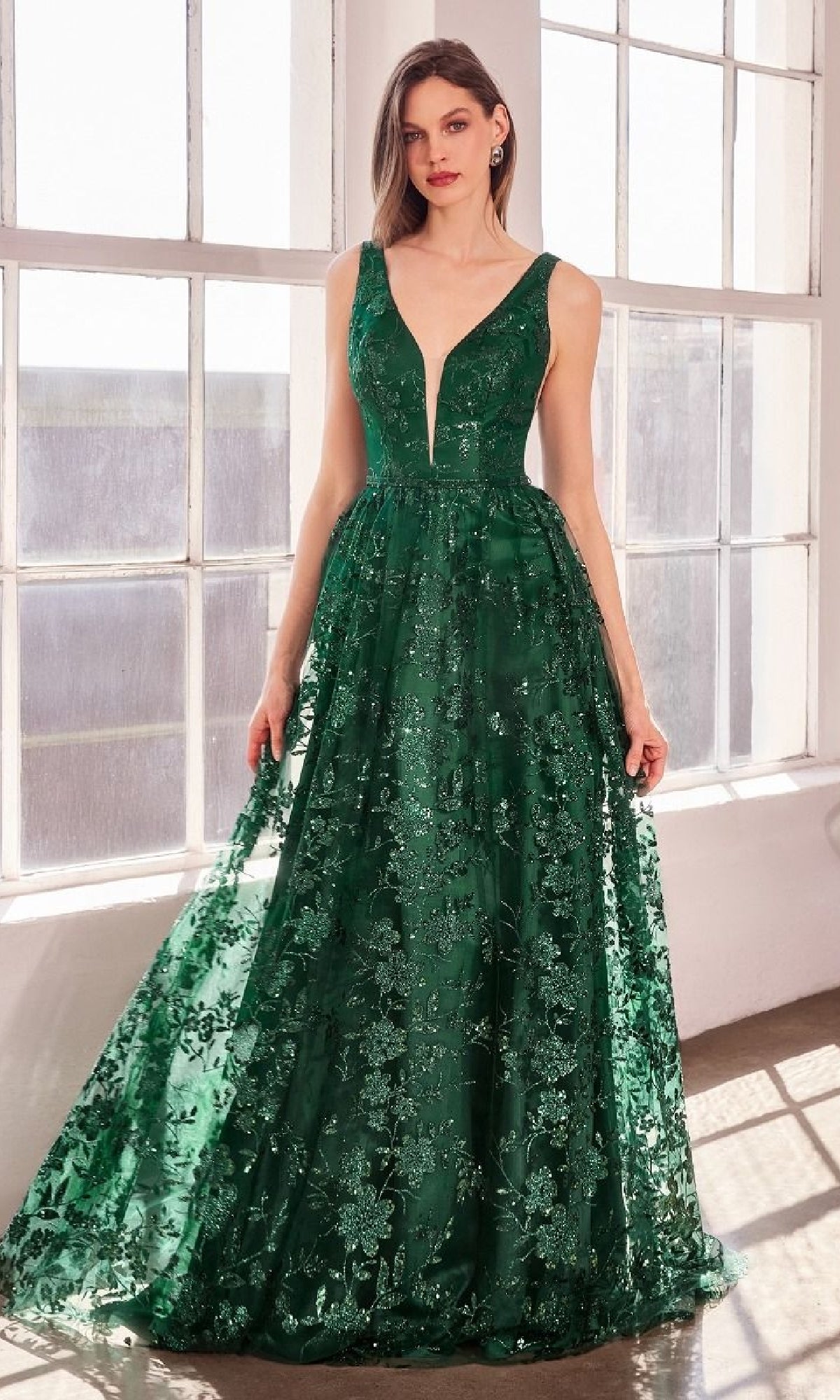 A woman poses by sunlit windows in the Amoris T606, an embroidered-lace long prom dress featuring a sleeveless deep V-neck and green floral details—an affordable, elegant choice for formal events.